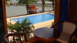 Habitación con vista a una piscina, palmeras y un muelle distante.