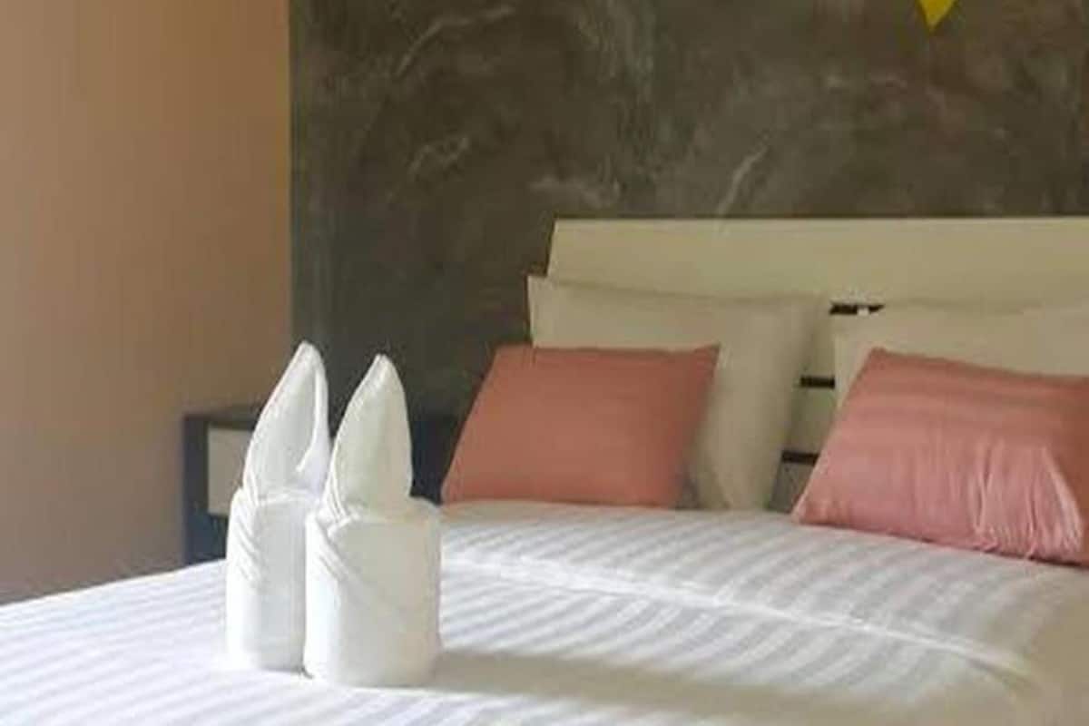 Una cama bien hecha con sábanas blancas y almohadas rosadas, una pared de mármol y una decoración con flores amarillas.