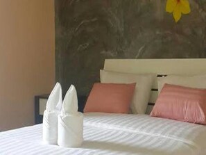 A neatly made bed with white linens and pink pillows, a marble wall, and a yellow flower decoration. - Nalin Place Ranong (Ranong)