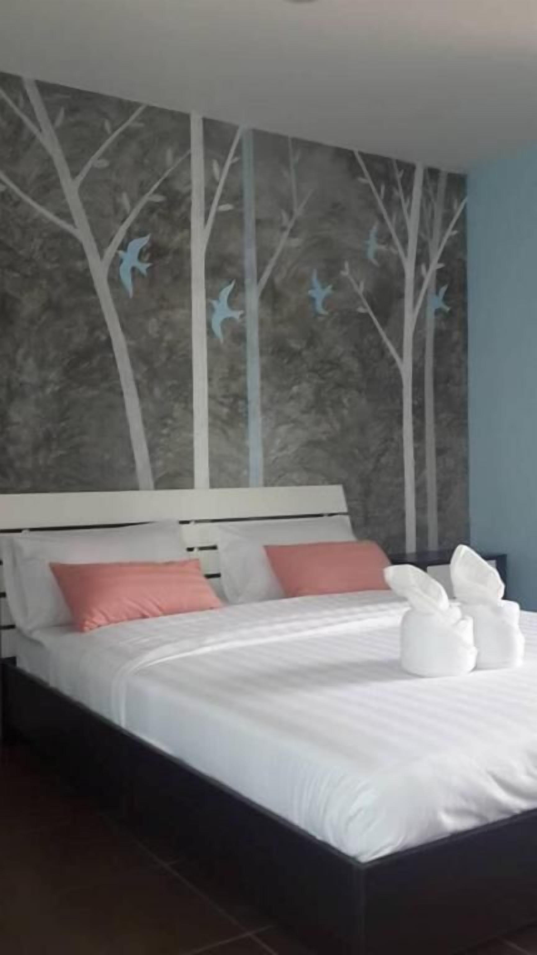 Una cama bien tendida con almohadas blancas y rosadas, un cabecero blanco y un mural con árboles y pájaros.