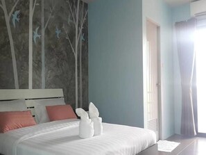 Un dormitorio con cama, almohadas, un mural en la pared y una ventana con cortinas.