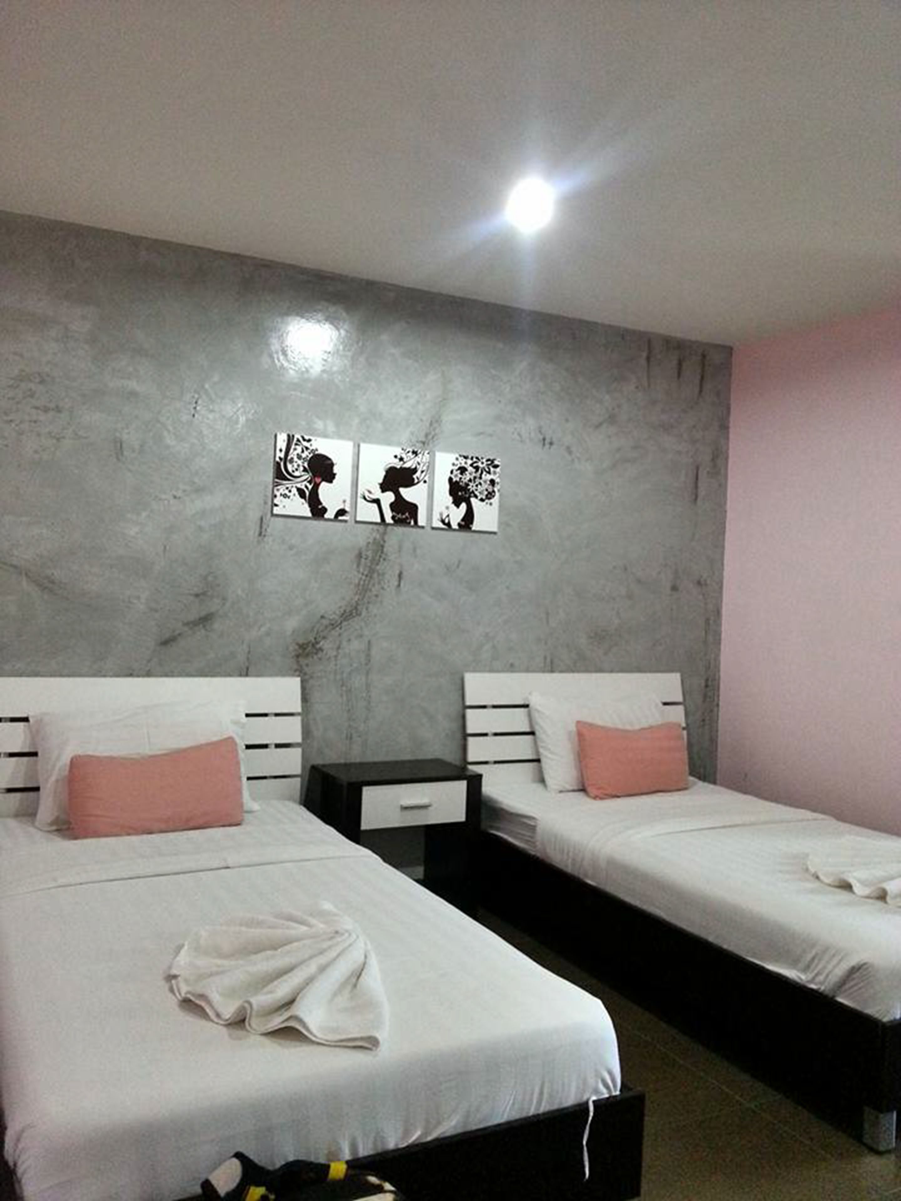 A hotel room with two beds, a nightstand, and a marble wall with three black and white artwork pieces.