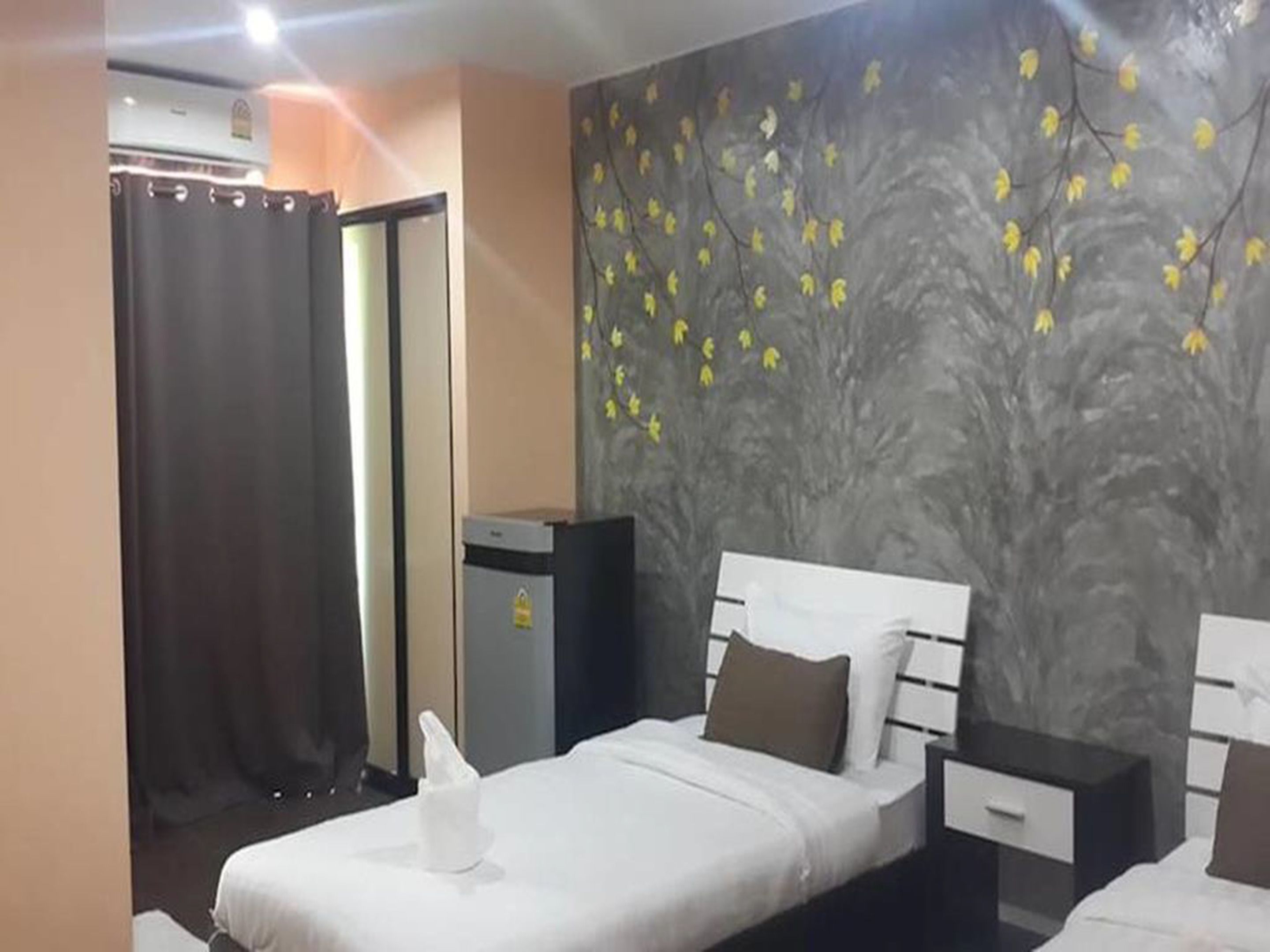 A hotel room with a bed, a nightstand, a wall-mounted heater, and a door with a curtain.