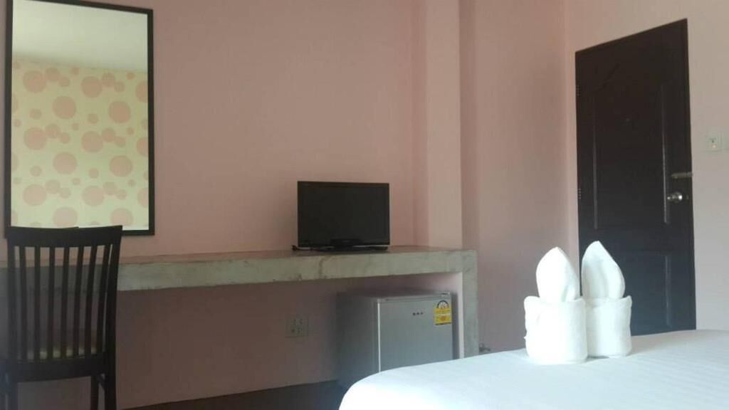 A hotel room with a bed, a desk with a computer, a chair, a small refrigerator, and a door.
