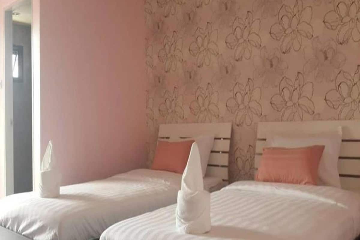 Habitación de hotel con dos camas, cada una con una colcha blanca y una almohada rosa. Las paredes tienen un estampado floral.