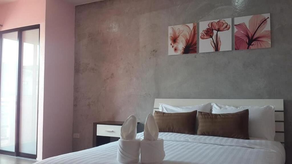 Habitación de hotel con cama, almohadas, mesita de noche y un cuadro floral en la pared.