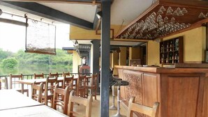 A restaurant with wooden tables and chairs, a bar area with stools, and a view of a lake. - Lake Serenity Boutique Hotel (Kuruwita)