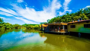 A riverside house with a balcony, surrounded by lush greenery and a clear blue sky. - Lake Serenity Boutique Hotel (Kuruwita)