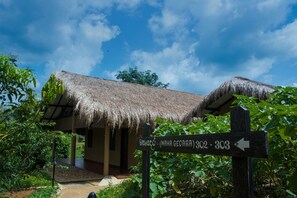 A thatched-roof structure with a sign indicating directions to 'Maha Gedara' and room numbers 302-303.