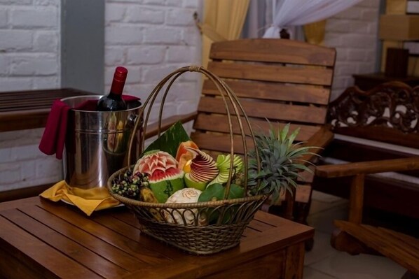 A wooden table with a metal bucket containing a bottle, a woven basket with fruits and vegetables, and a red cloth.