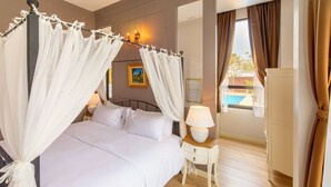 A bedroom with a four-poster bed, a bedside table with a lamp, and a view of an outdoor swimming pool. - FarmHouse Hotel Ranong (Ranong)