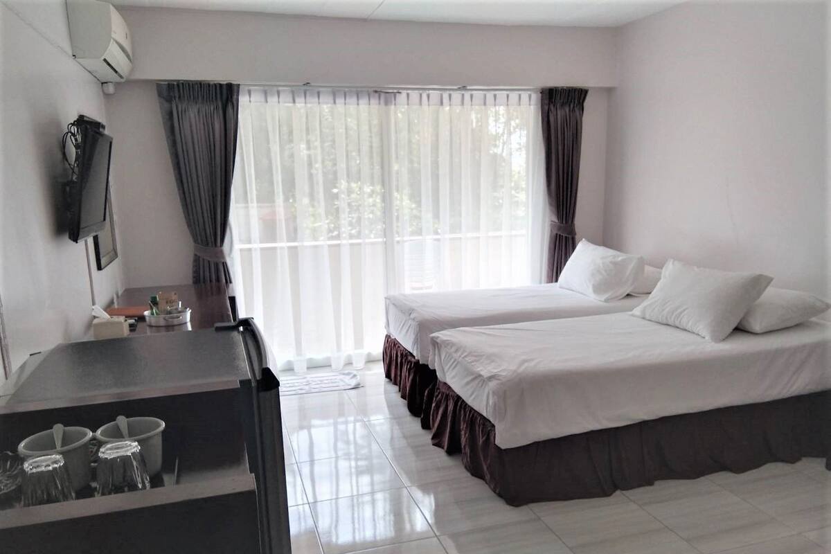A hotel room with two beds, a desk with a chair, a flat-screen TV, and a window with curtains.