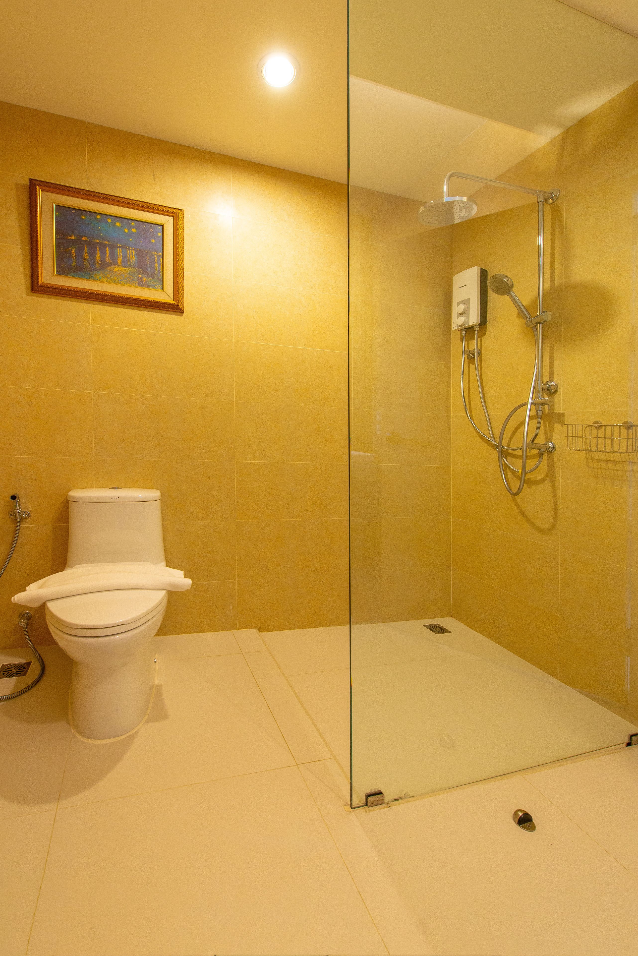 A bathroom with a glass shower enclosure, a toilet, and a framed picture on the wall.