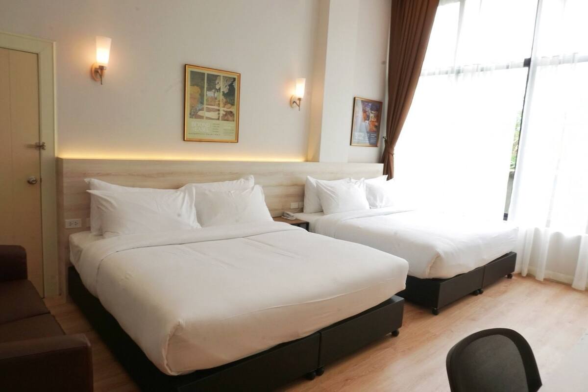 A hotel room with two beds, a wooden floor, a desk, and a chair.