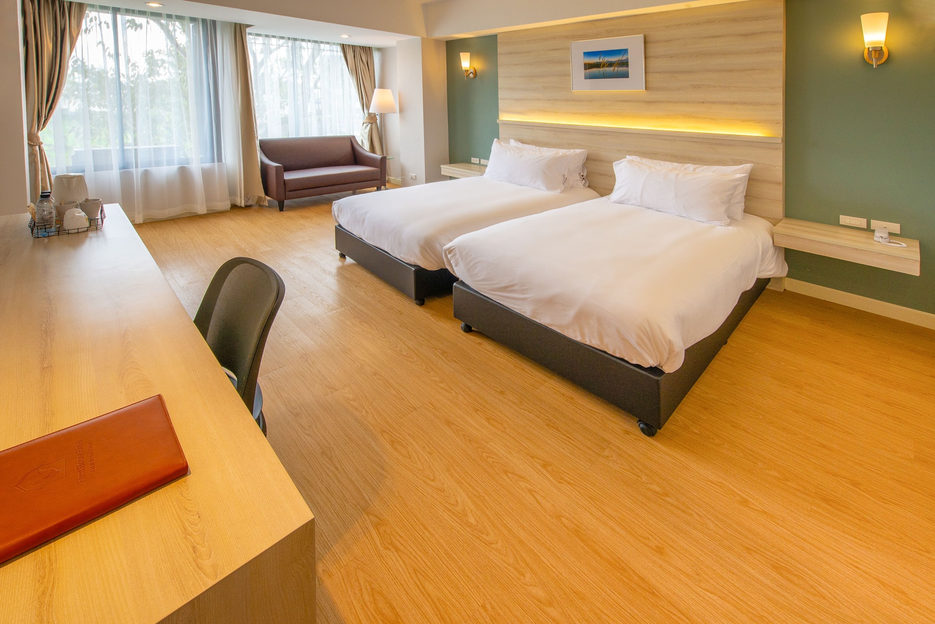 A hotel room with two beds, a desk, a chair, and a sofa.