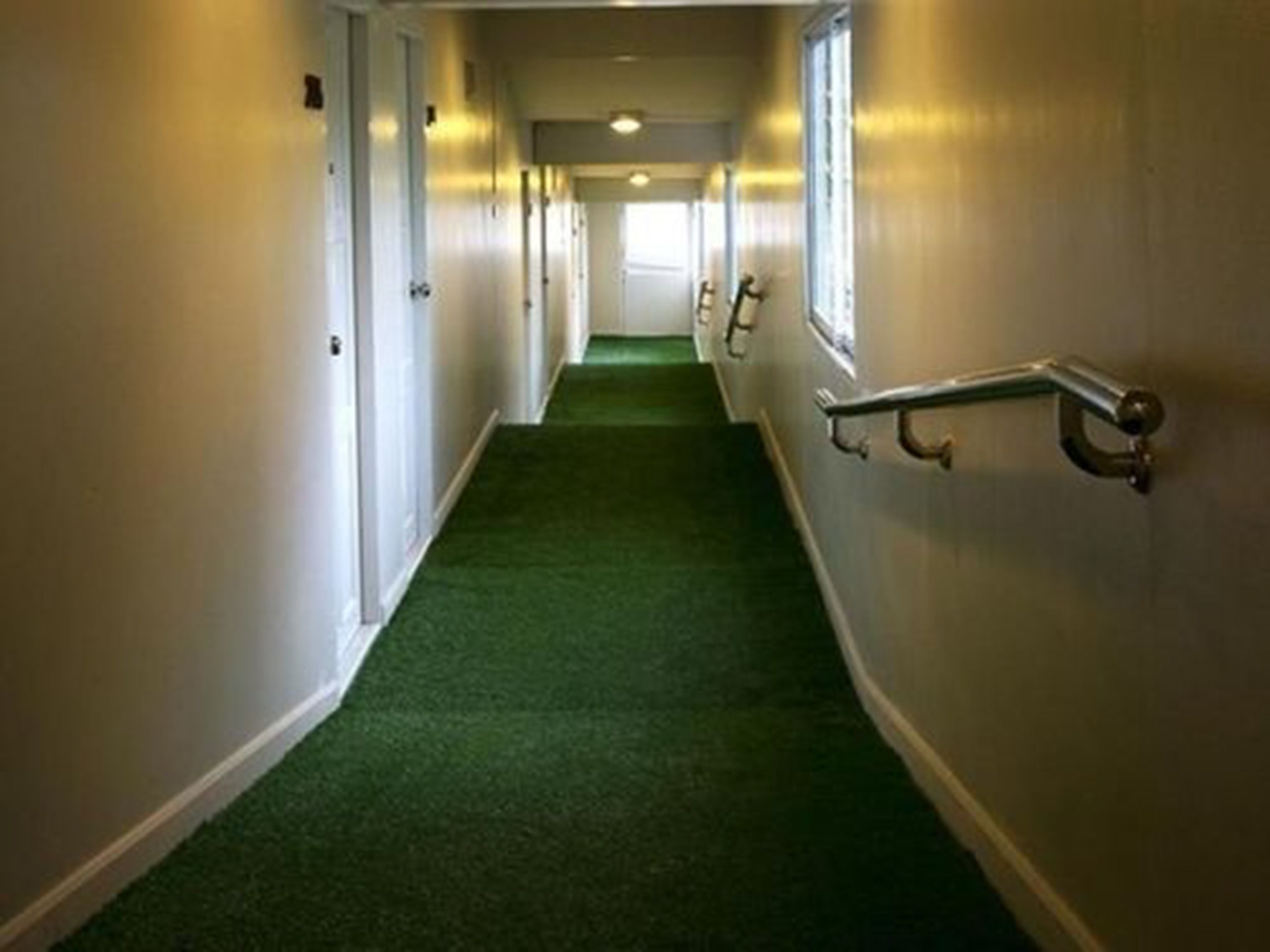 Un pasillo con alfombra verde, paredes blancas y una barandilla a la derecha.