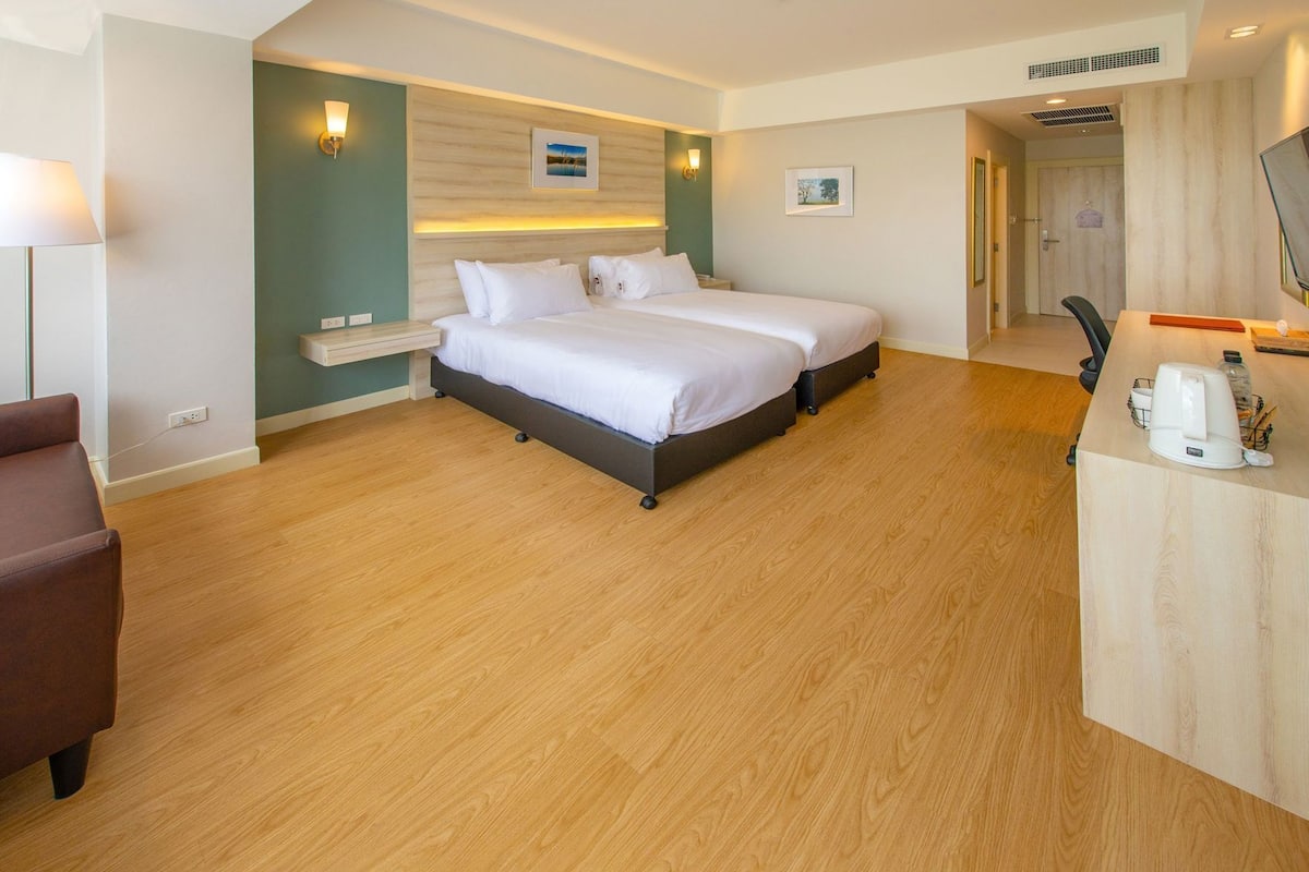 A hotel room with two beds, a desk, a chair, and a small seating area.