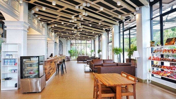A spacious lobby with a wooden reception desk, seating area, and a snack bar. - FarmHouse Hotel Ranong (Ranong)