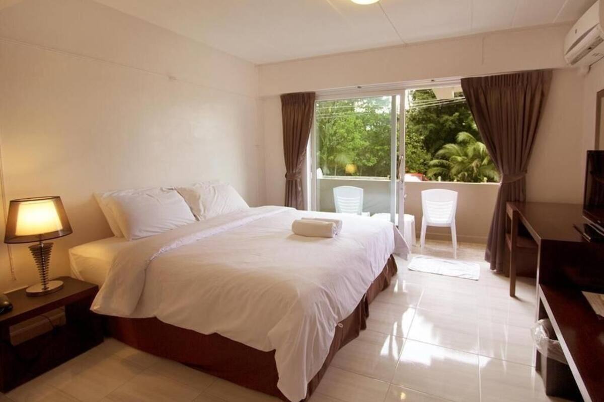 A hotel room with a bed, a desk, a chair, a TV, and a balcony with curtains.