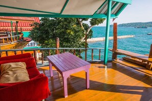 A wooden deck with a red sofa and a purple table, overlooking a turquoise sea and a red-roofed building. - Rimtalay Resort Koh Si Chang (Ko Sichang)