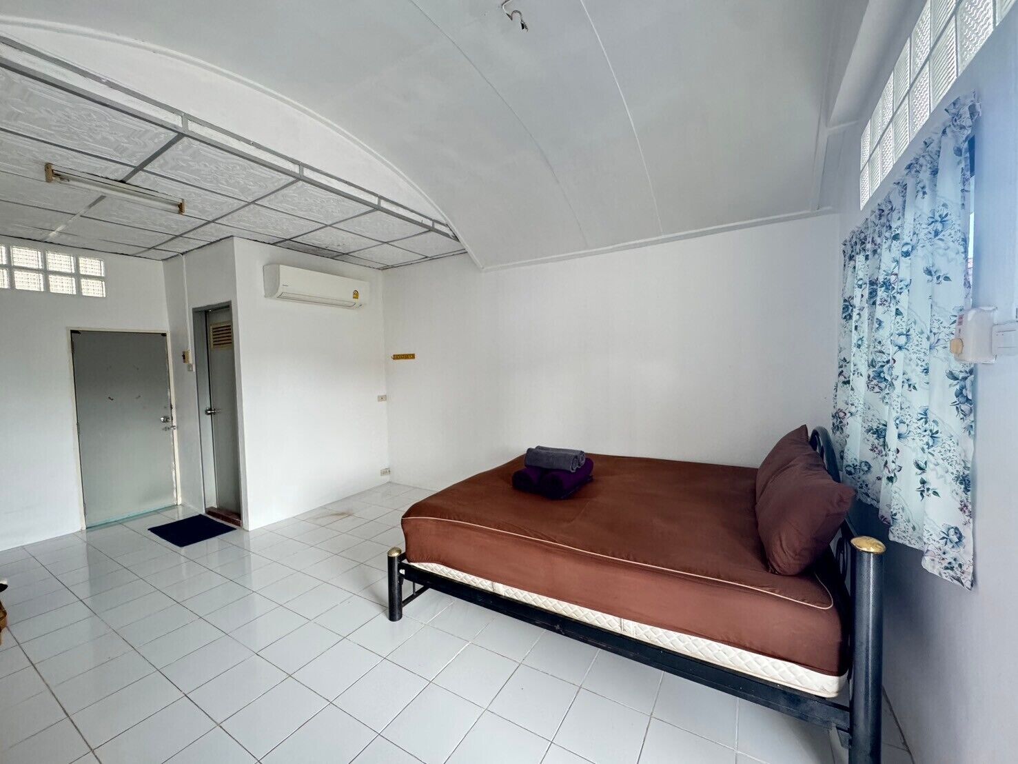 A room with a bed, a door, an air conditioning unit, and a window with curtains.