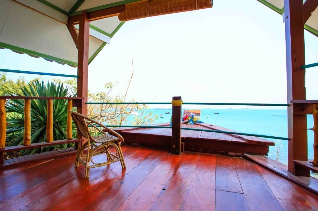 A wooden deck with a wicker chair, overlooking a calm sea with boats.