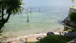 A clear beach with calm water, some trees, and a concrete structure. - Rimtalay Resort Koh Si Chang (Ko Sichang)