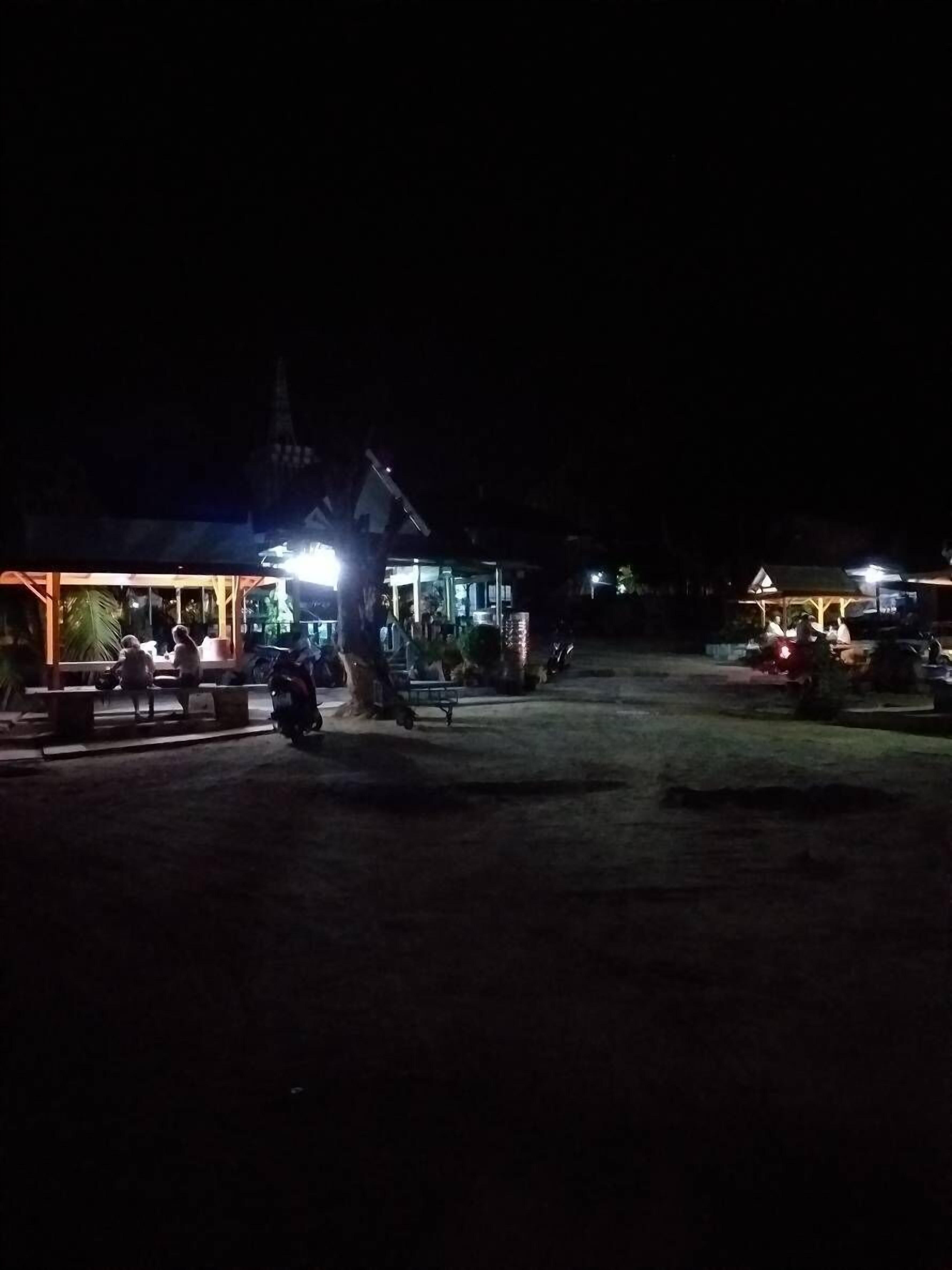 A nighttime view of a building with a lit entrance and a covered area with benches.