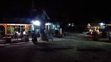 A nighttime view of a building with a lit entrance and a covered area with benches.