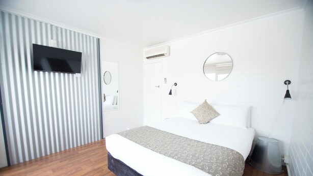 A modern bedroom with a large bed, a TV mounted on the wall, an air conditioning unit, and a mirror. - Siesta Central Apartments (Sale)