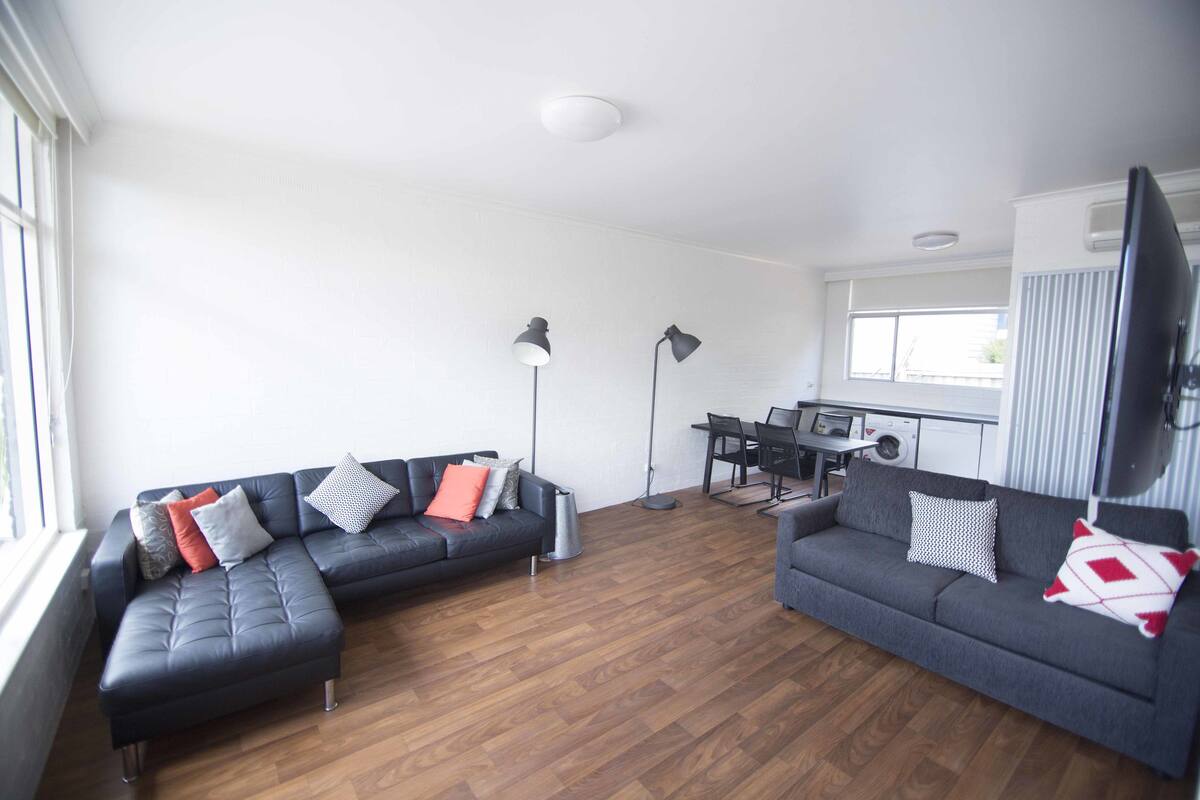 A modern living room with two grey sofas, a dining table, and a kitchen area.