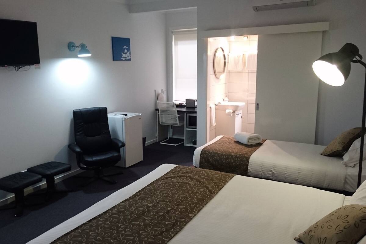 A hotel room with two beds, a desk, a chair, a TV, and a bathroom visible through an open door.