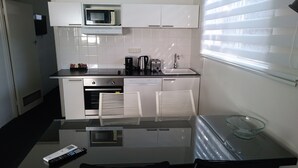A modern kitchen with white cabinets, a microwave, a coffee maker, and a toaster. There is a glass table with a remote control and a glass bowl. - Siesta Central Apartments (Sale)