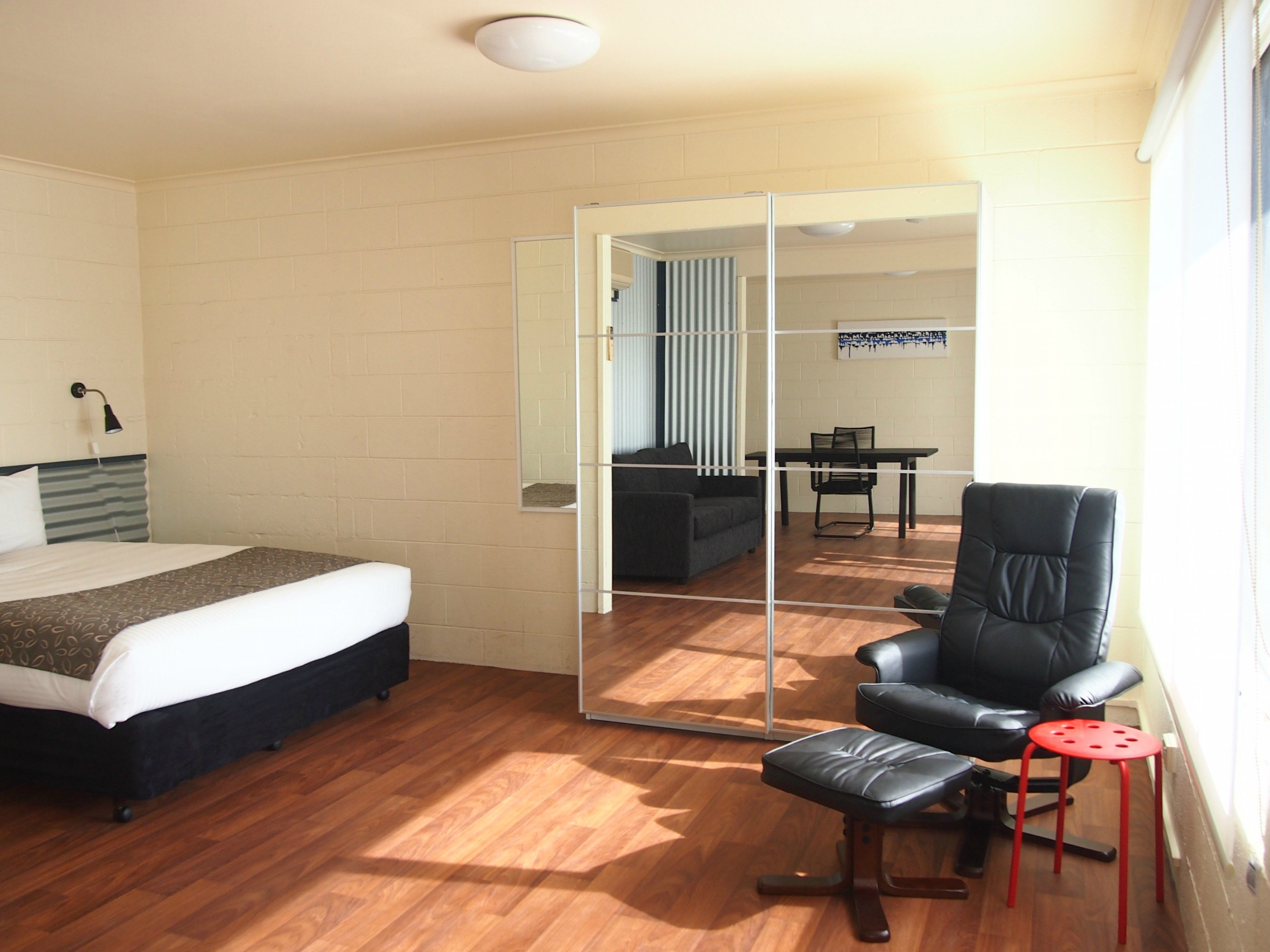 Una habitación de hotel con una cama, una silla, una mesita y un espejo.