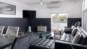 A modern living room with a glass-top table, black leather sofa, and white wicker chairs. - Siesta Central Apartments (Sale)