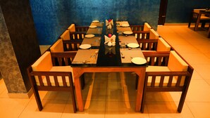 A dining area with a long table set for multiple people, surrounded by wooden chairs with cushions.