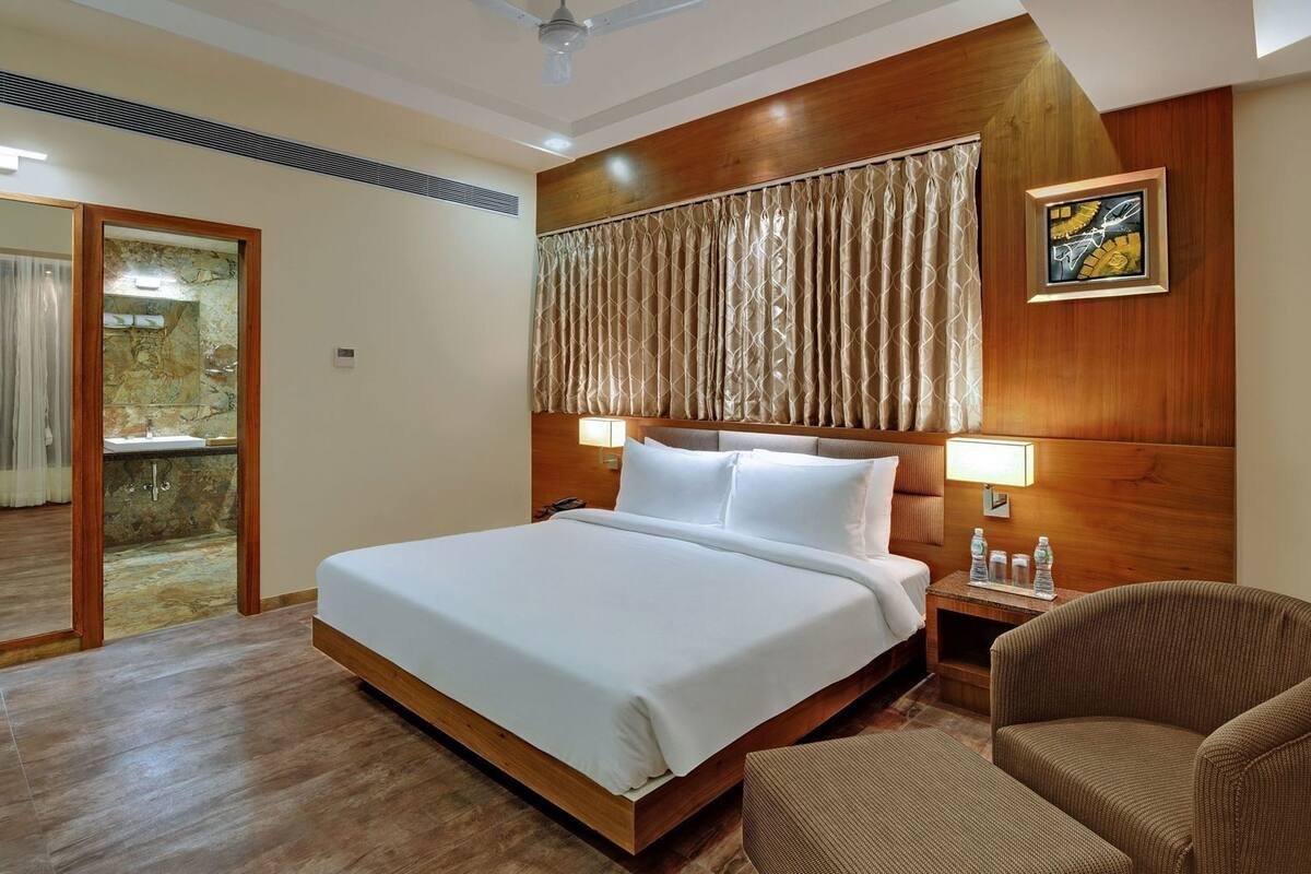 A hotel room with a large bed, a wooden headboard, a nightstand with a lamp, a chair, and a mirror.