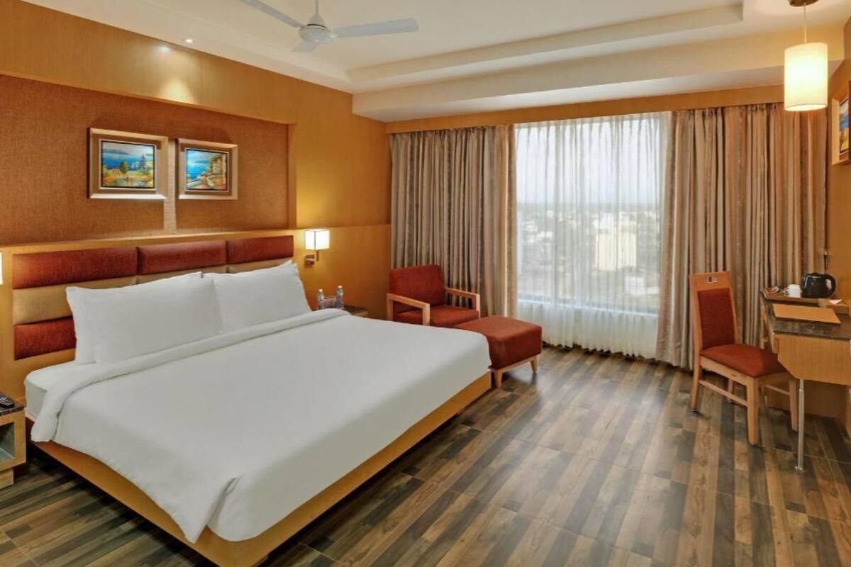 A hotel room with a large bed, a desk, two chairs, a ceiling fan, and a window with curtains.