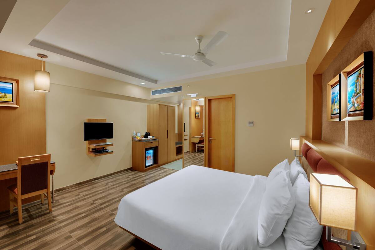 A hotel room with a bed, desk, chair, TV, and a ceiling fan.