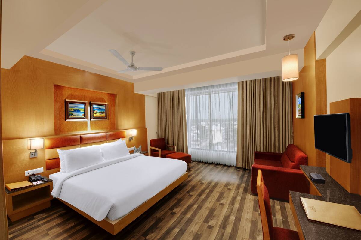 A hotel room with a large bed, a desk with a chair, a TV, and a window with curtains.