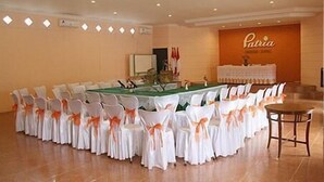 A conference room with a long table surrounded by chairs with white covers and orange sashes, a podium, and a wall with a sign reading "Patria". - Patria Garden Hotel (Blitar)