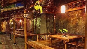 A rustic wooden structure with a bench and a table, surrounded by stone walls and hanging lights. - Patria Garden Hotel (Blitar)