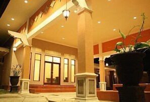 Un hall d’hôtel avec une grande colonne centrale, un comptoir d’accueil et une plante en pot.