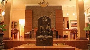 A lobby with a central Buddha statue, wooden columns, and potted plants. - Patria Garden Hotel (Blitar)