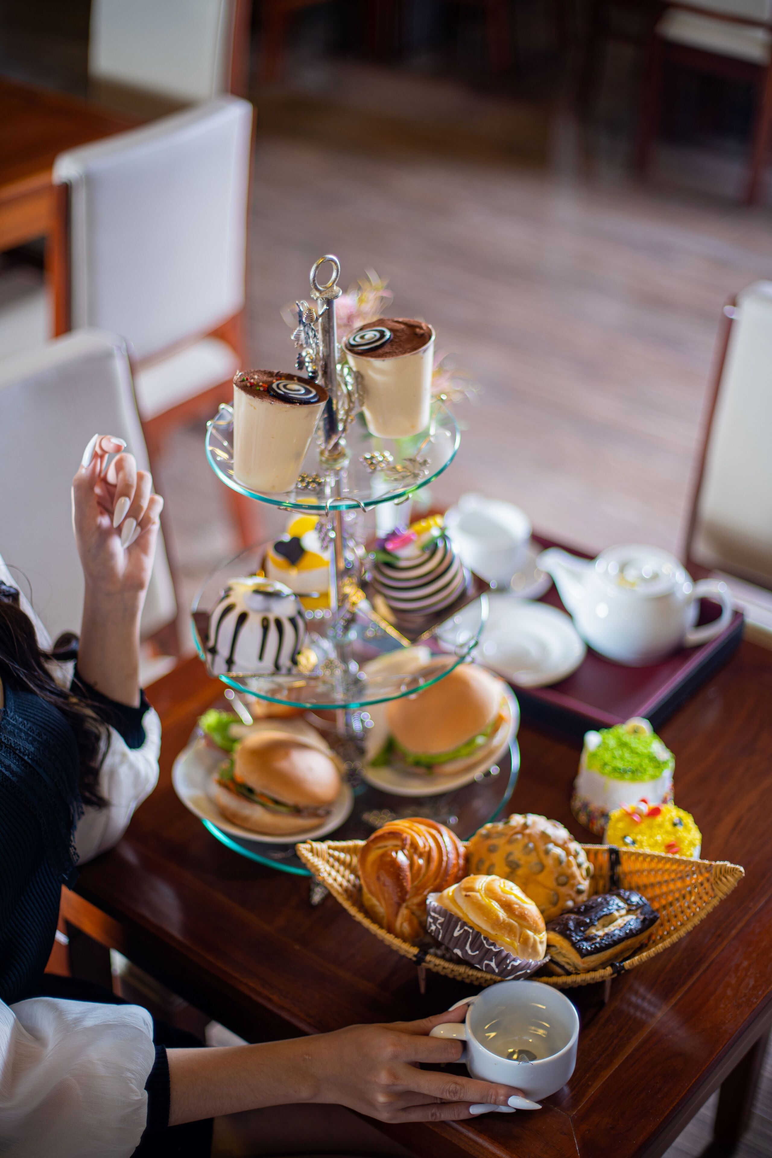 A three-tiered dessert stand with various pastries and a teapot on a wooden table.