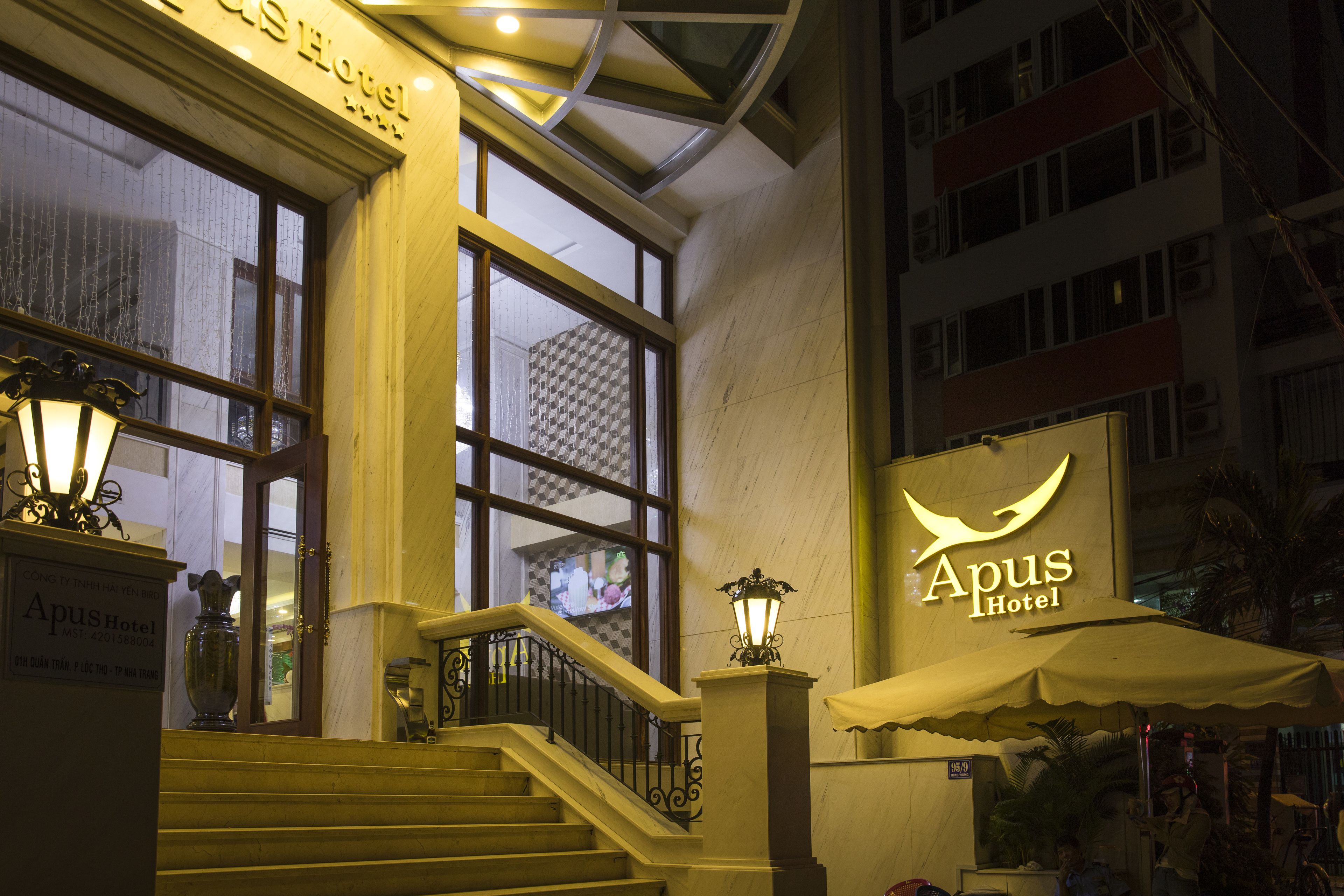 A hotel entrance with a staircase, a sign reading "Apus Hotel", and a large window with a view of the cityscape.