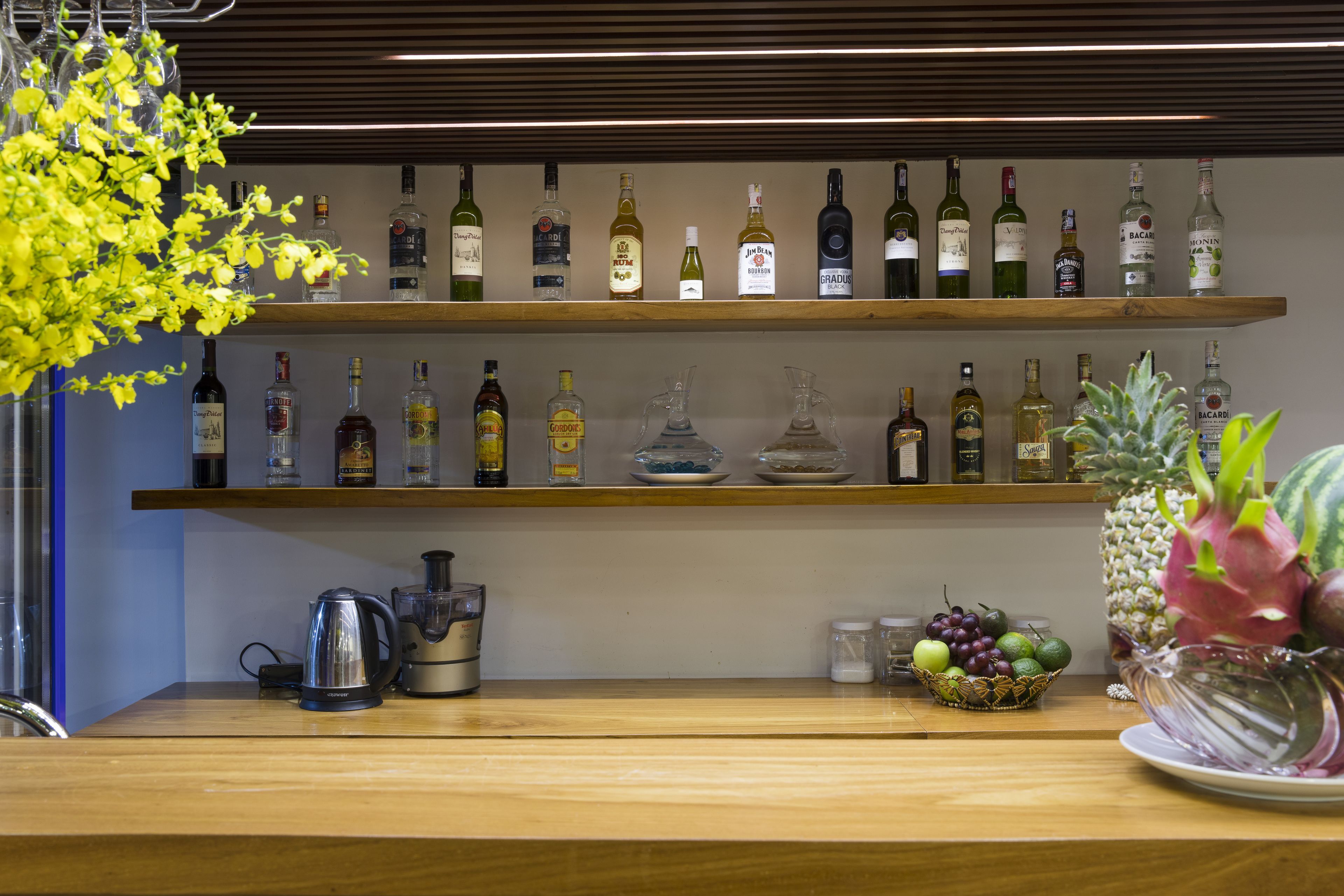 Angolo bar con scaffali pieni di bottiglie di liquore, una macchina per caffè e una ciotola di frutta.