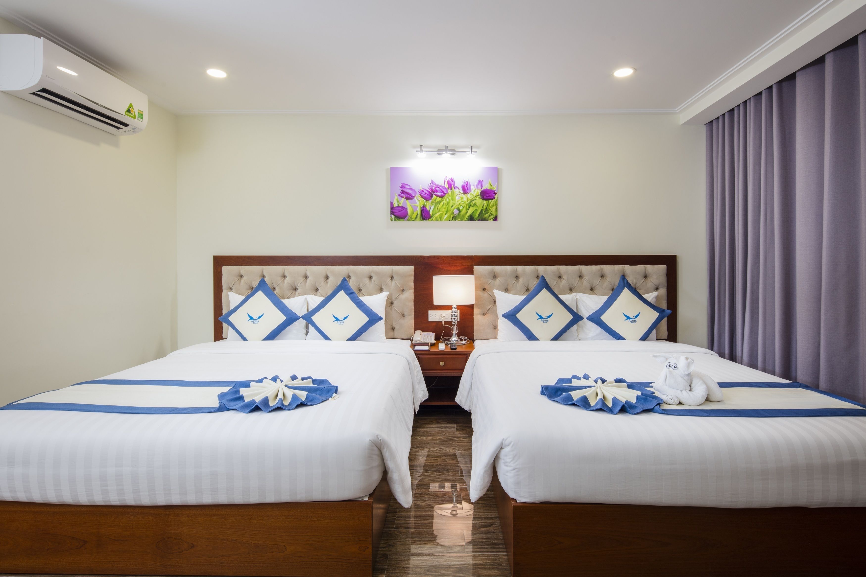 Une chambre d’hôtel avec deux lits, une table de chevet, une lampe et un climatiseur fixé au mur.
