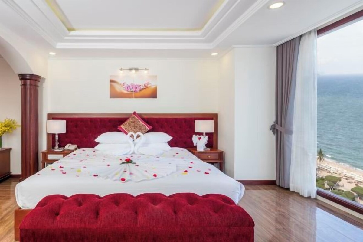 Habitación de hotel con una cama grande, cabecera roja, un cuadro sobre la cama y vista al mar.