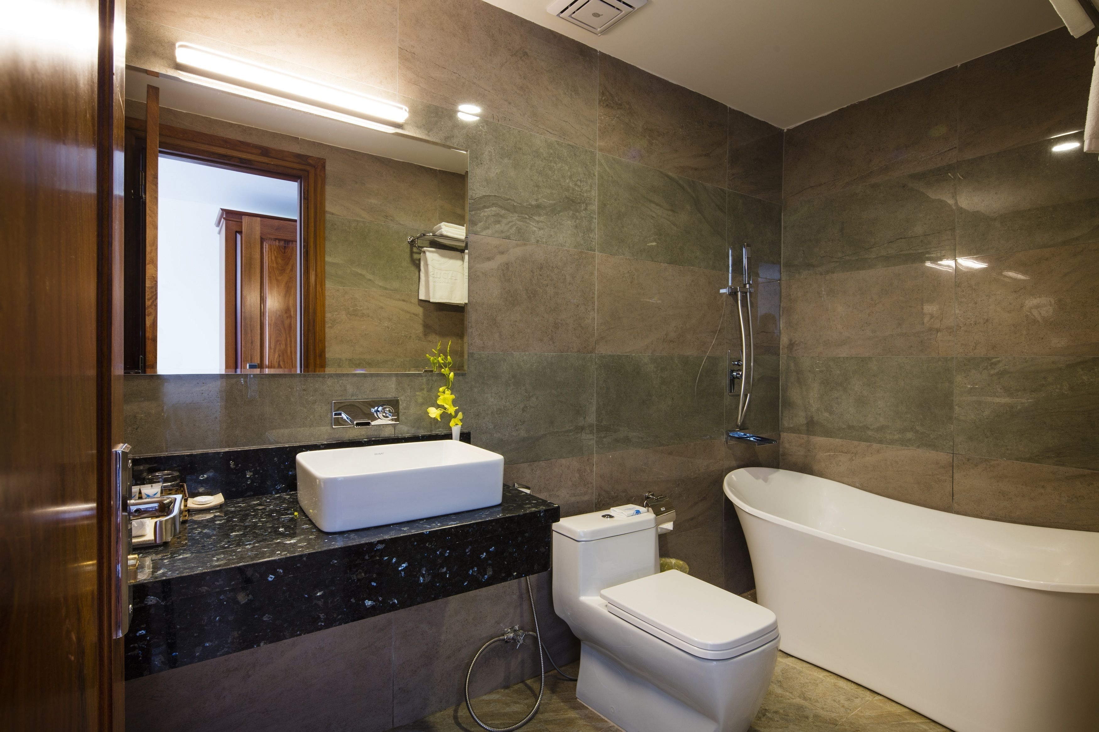 A modern bathroom with a freestanding bathtub, a toilet, and a sink with a marble countertop.
